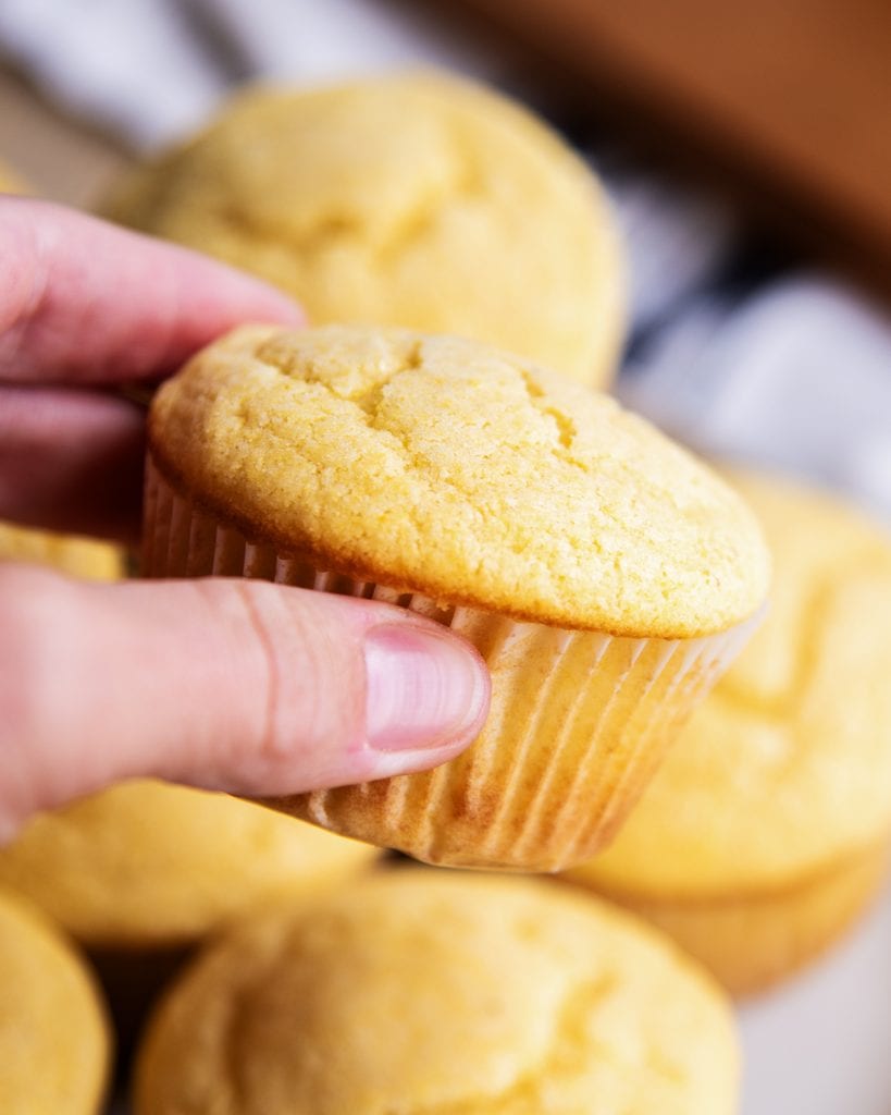 A hand holding a cornbread muffin with a paper liner.