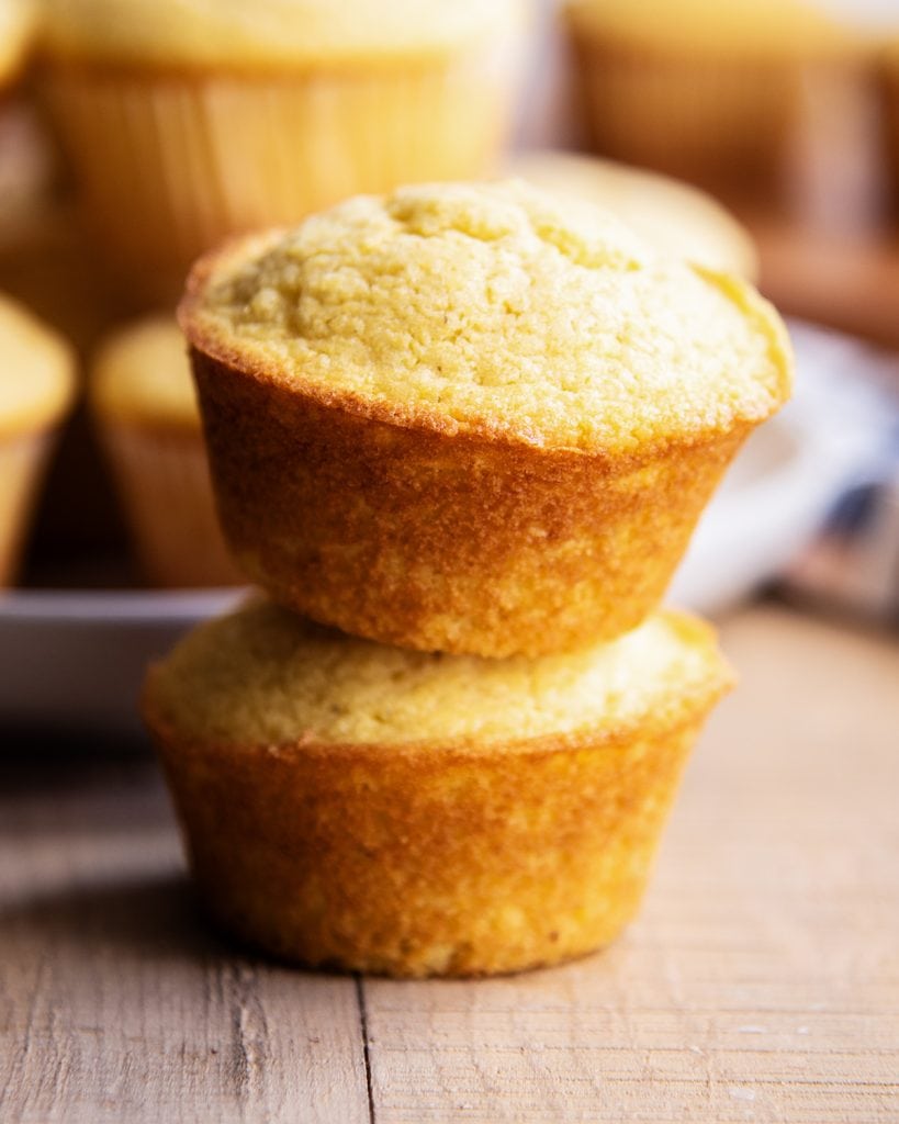 A stack of two golden cornbread muffins on a wooden table.