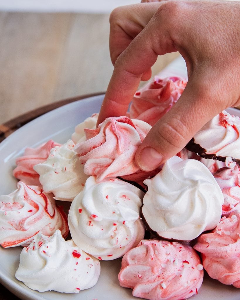 A hand lifting a meringue cookie of a plate of them.
