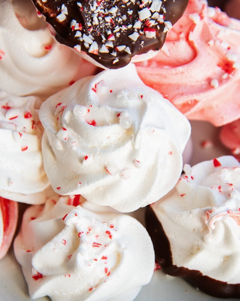 A close up of a white meringue cookie in a pile, topped with candy cane pieces.