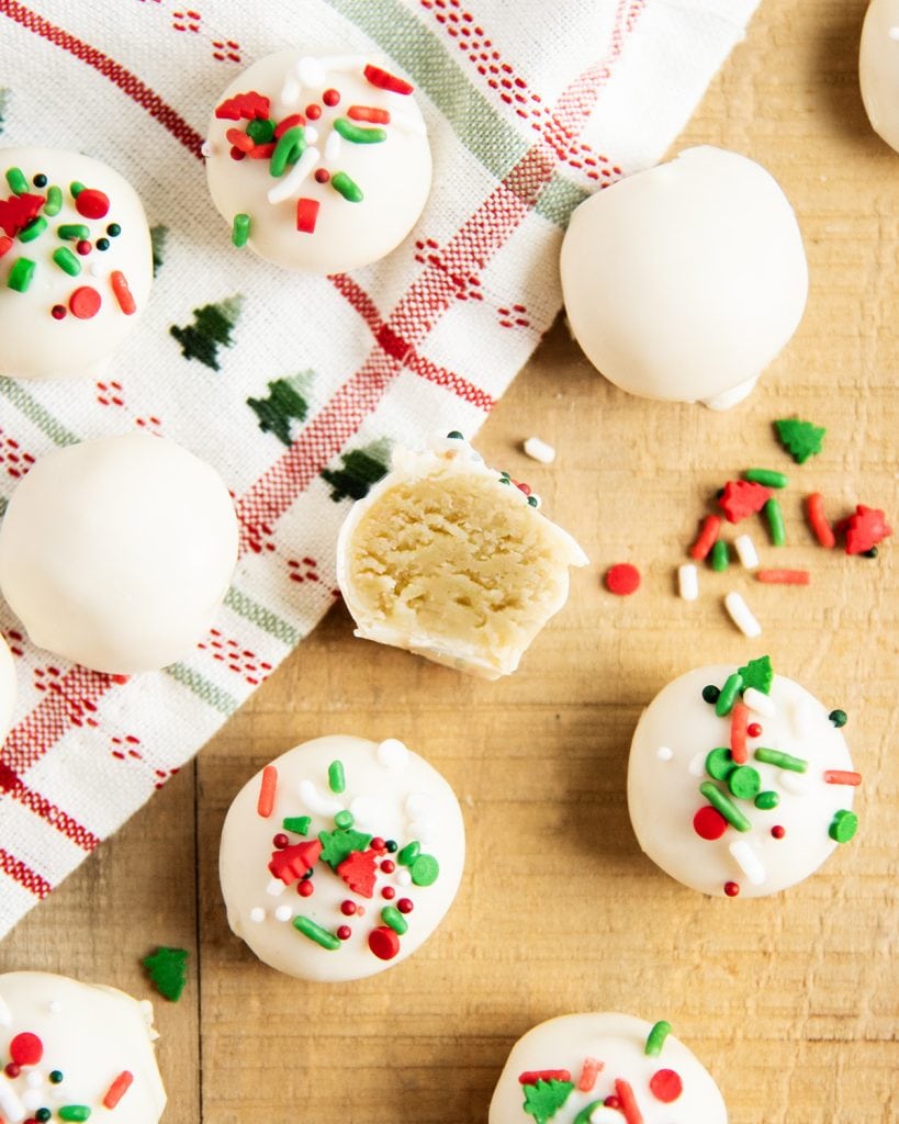 White Chocolate Coated Sugar Cookie Truffles on a wooden table. One is cut in half showing the sugar cookie filling.