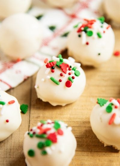 Sugar cookie truffles on a wooden table topped with Christmas sprinkles.