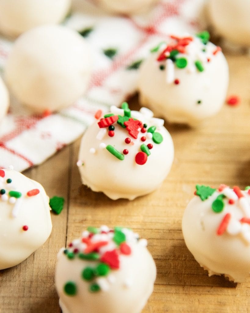Sugar cookie truffles on a wooden table topped with Christmas sprinkles.