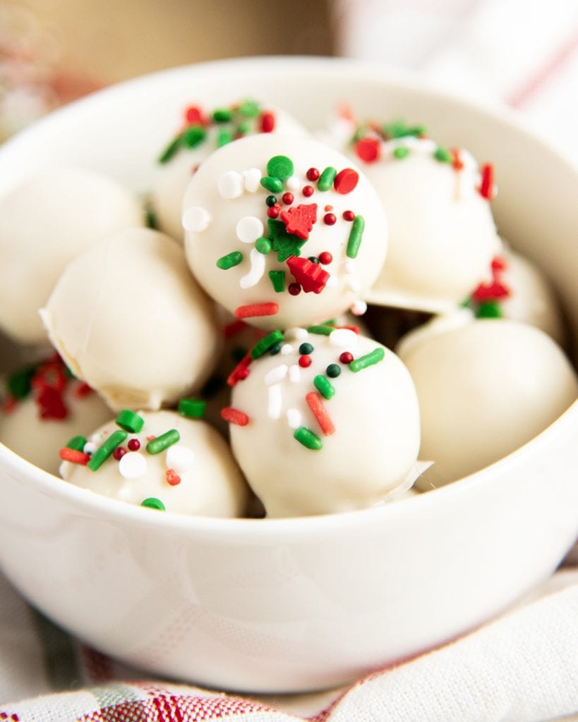 A close up of white chocolate sugar cookie truffles in a bowl, topped with Christmas sprinkles.
