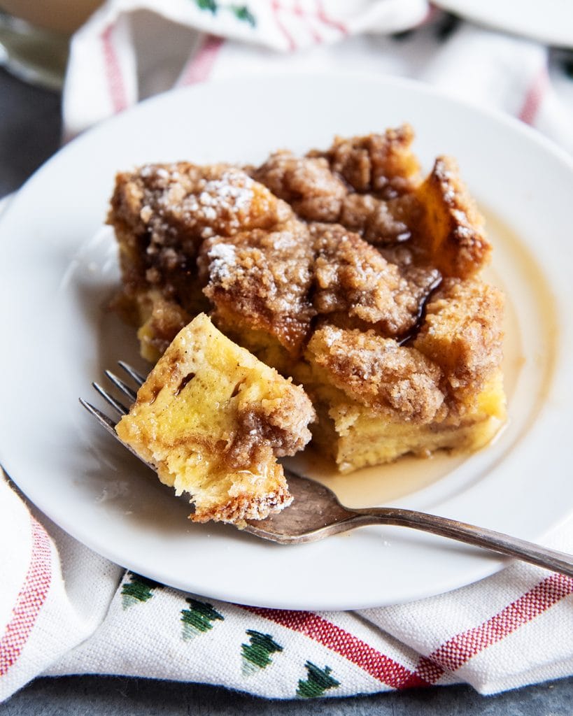 A bite of eggnog french toast casserole on a fork next to a serving of it on a plate.