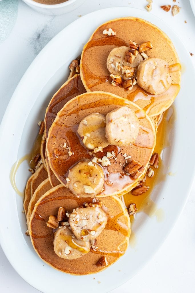 An overhead photo of a platter of pancakes with pecan butter on top.
