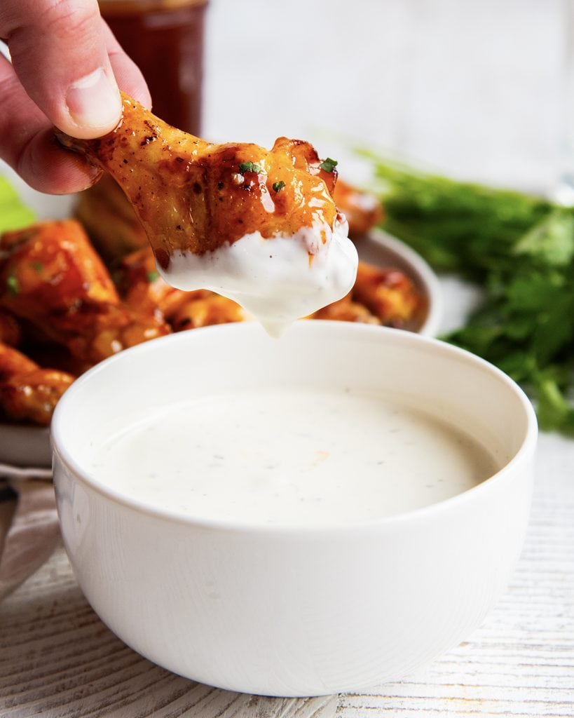 A and holding a buffalo chicken wing partially coated in ranch dressing.