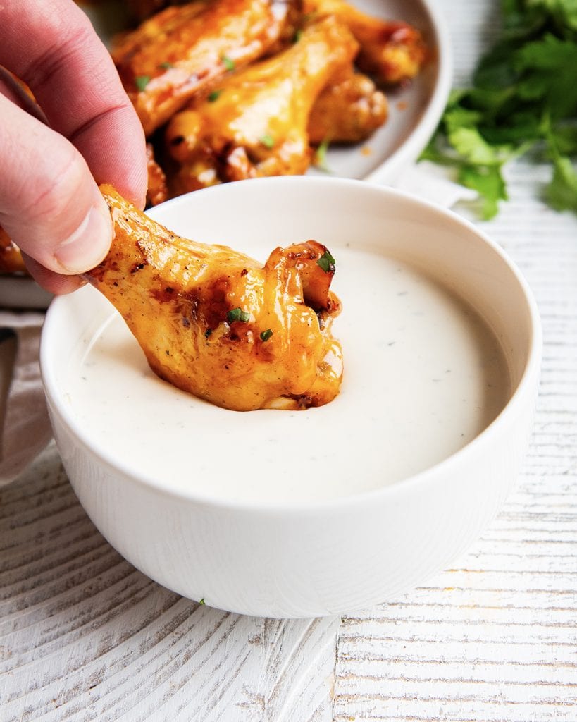 Fingers dipping a chicken wing into a bowl of ranch dressing.