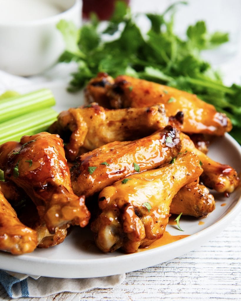 A plate of honey buffalo chicken wings on a plate with celery.