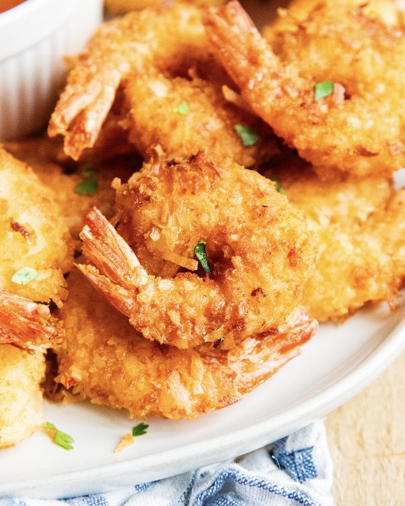 A close up of a piece of coconut shrimp with its tail on.