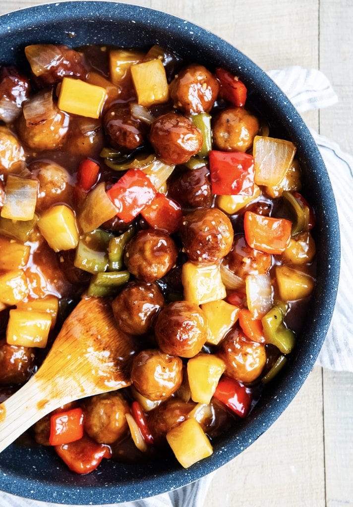 An overhead photo of a pan of sweet and sour meatballs with pineapples and bell peppers.