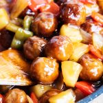 A pan of sweet and sour meatballs with a wooden spoon in there.