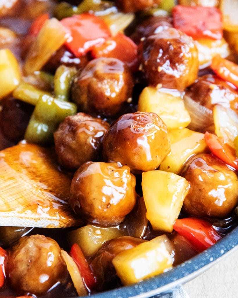 A pan of sweet and sour meatballs with a wooden spoon in there.