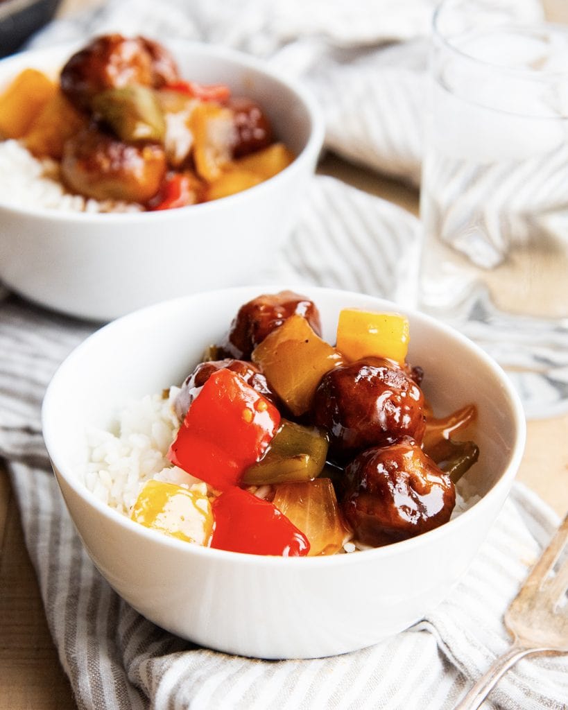 A bowl of sweet and sour meatballs, veggies, on top of rice.