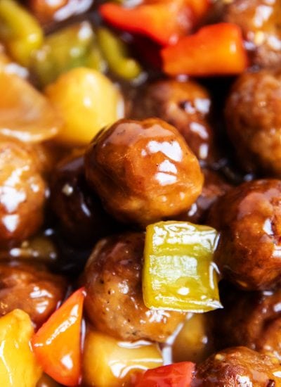 A close up of sweet and sour meatballs with green bell peppers and pineapple chunks.