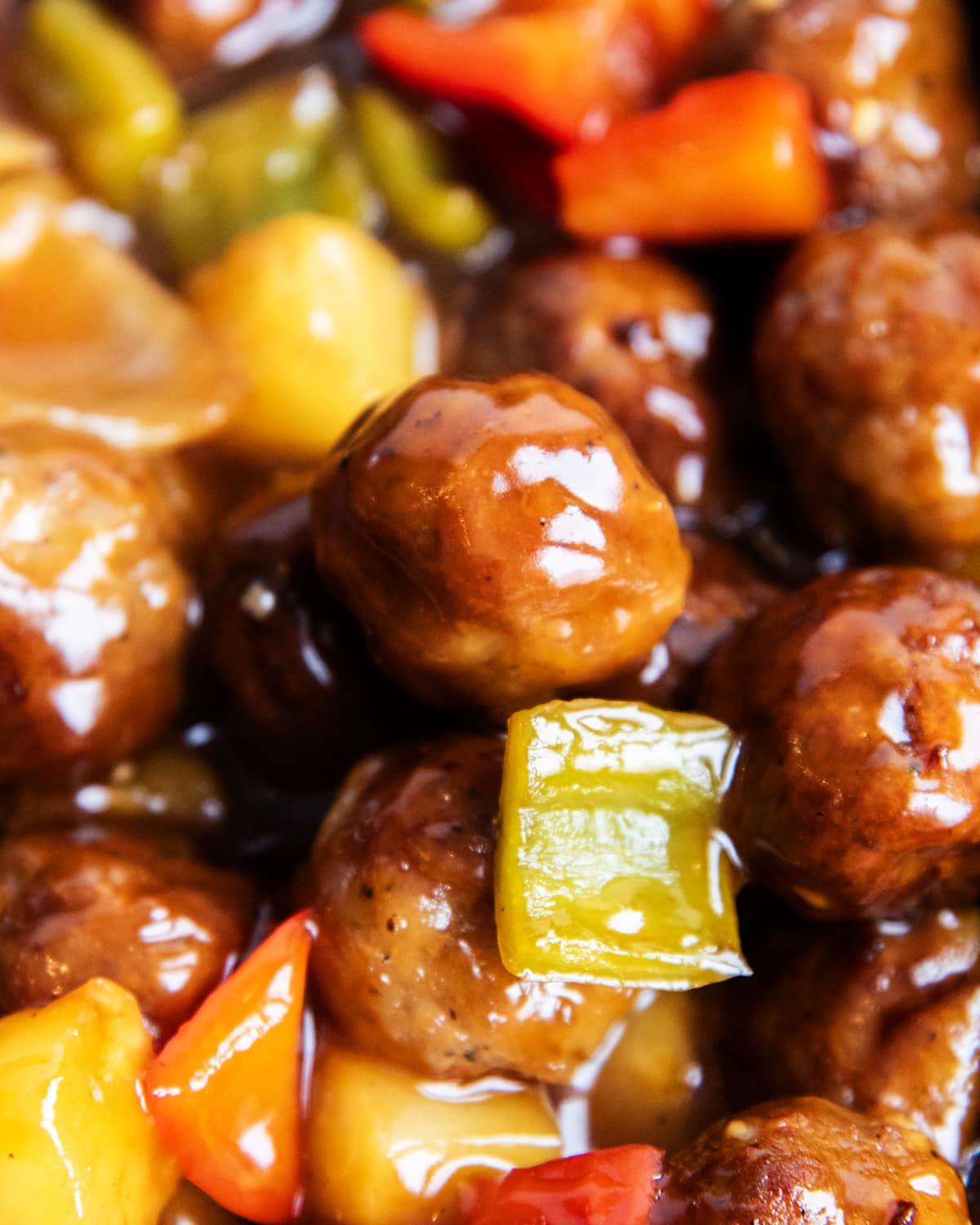 A close up of sweet and sour meatballs with green bell peppers and pineapple chunks.