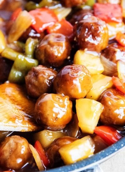 A pan of sweet and sour meatballs with a wooden spoon in there.