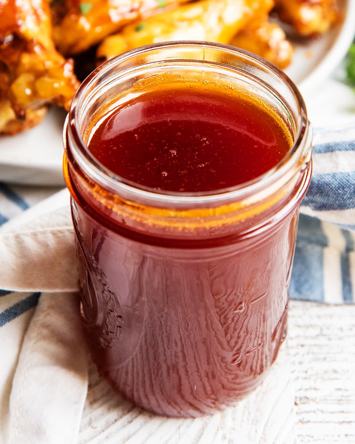 A glass jar full of homemade honey buffalo wing sauce, with a plate of wings behind it.