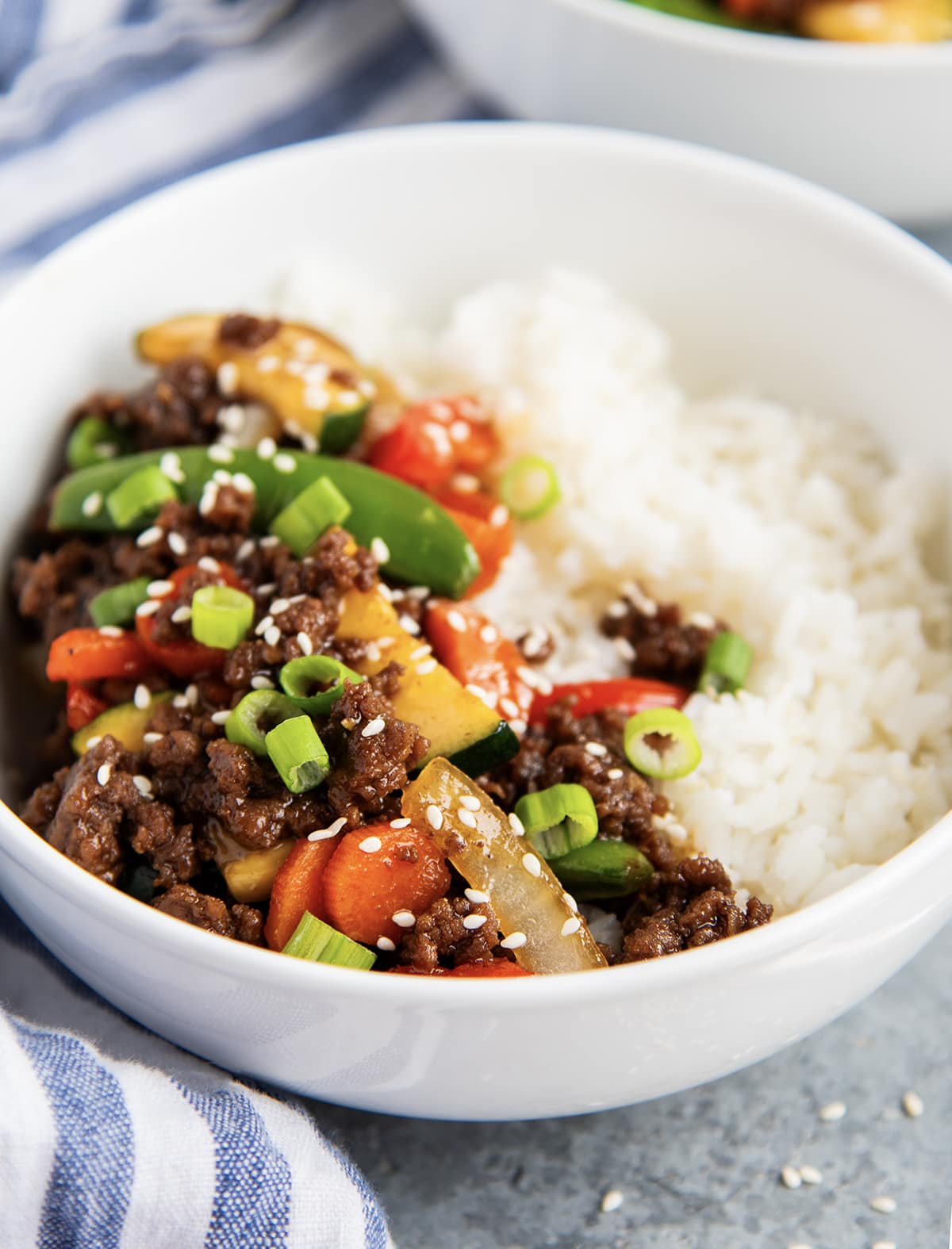 A bowl of white rice and Korean beef with vegetables, topped with sesame seeds.
