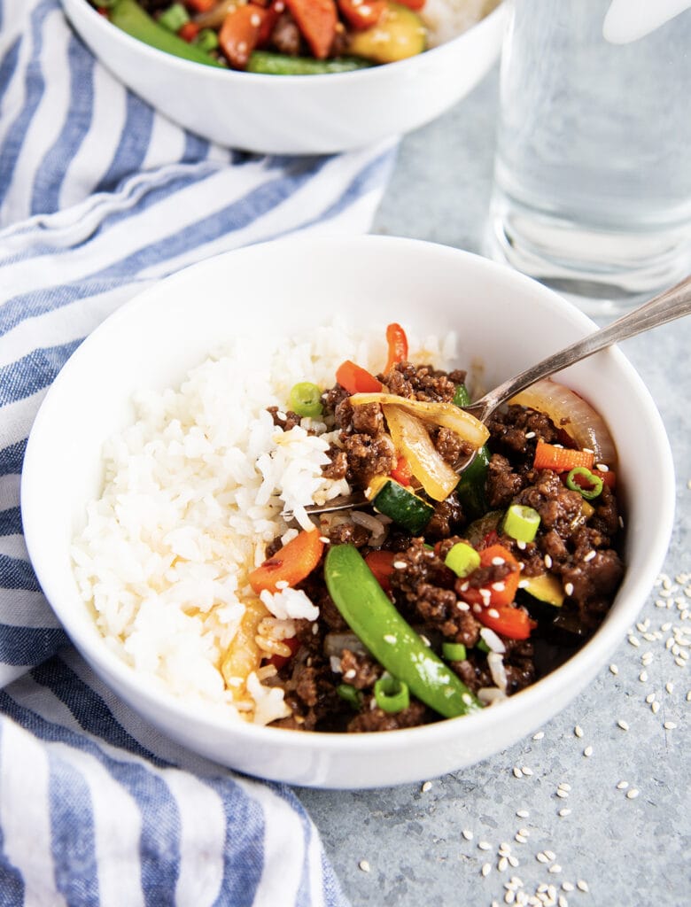 A bowl of Korean Beef and vegetables next to rice.