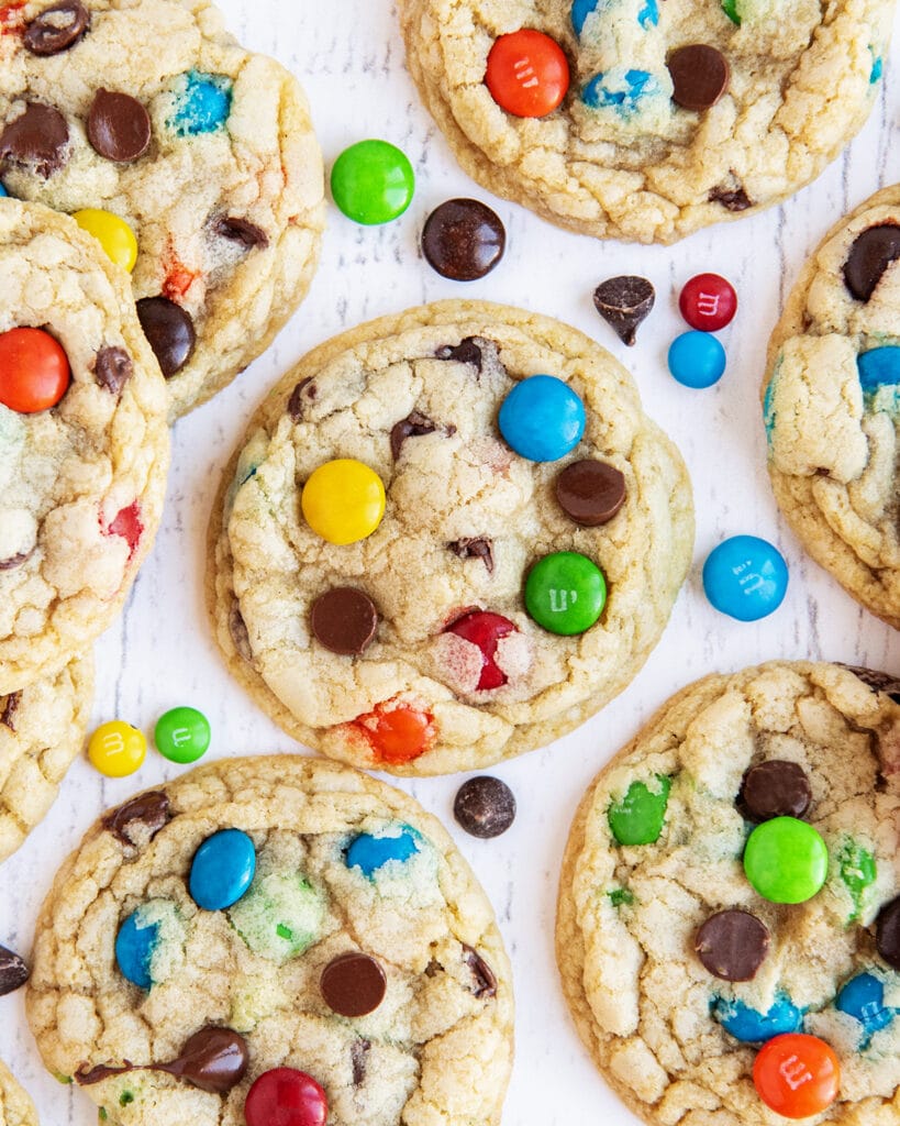 M&M and chocolate chip cookies on a white table, with M&Ms next to them.
