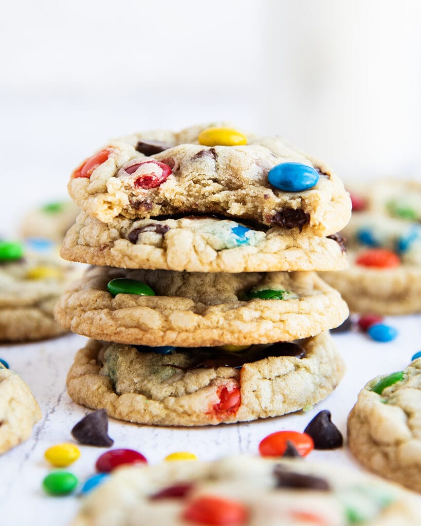 A stack of 4 M&M cookies, and the top cookie has a bite out of it.