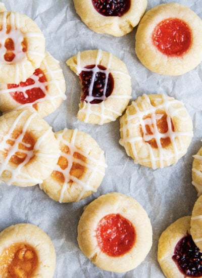 Thumbprint cookies filled with jam and randomly scattered on a piece of parchment paper.