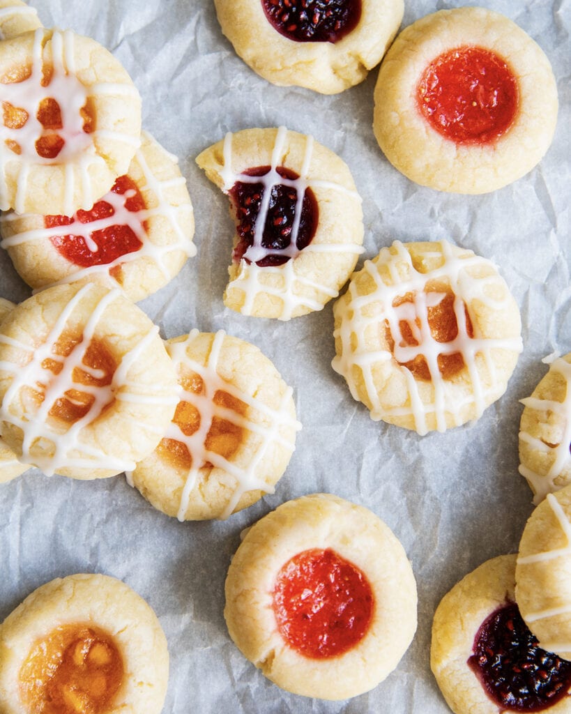 Thumbprint cookies filled with jam and randomly scattered on a piece of parchment paper.