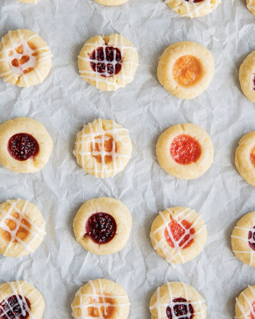 Rows of jam thumbprint cookies filled with different types of jam, and drizzled with icing.