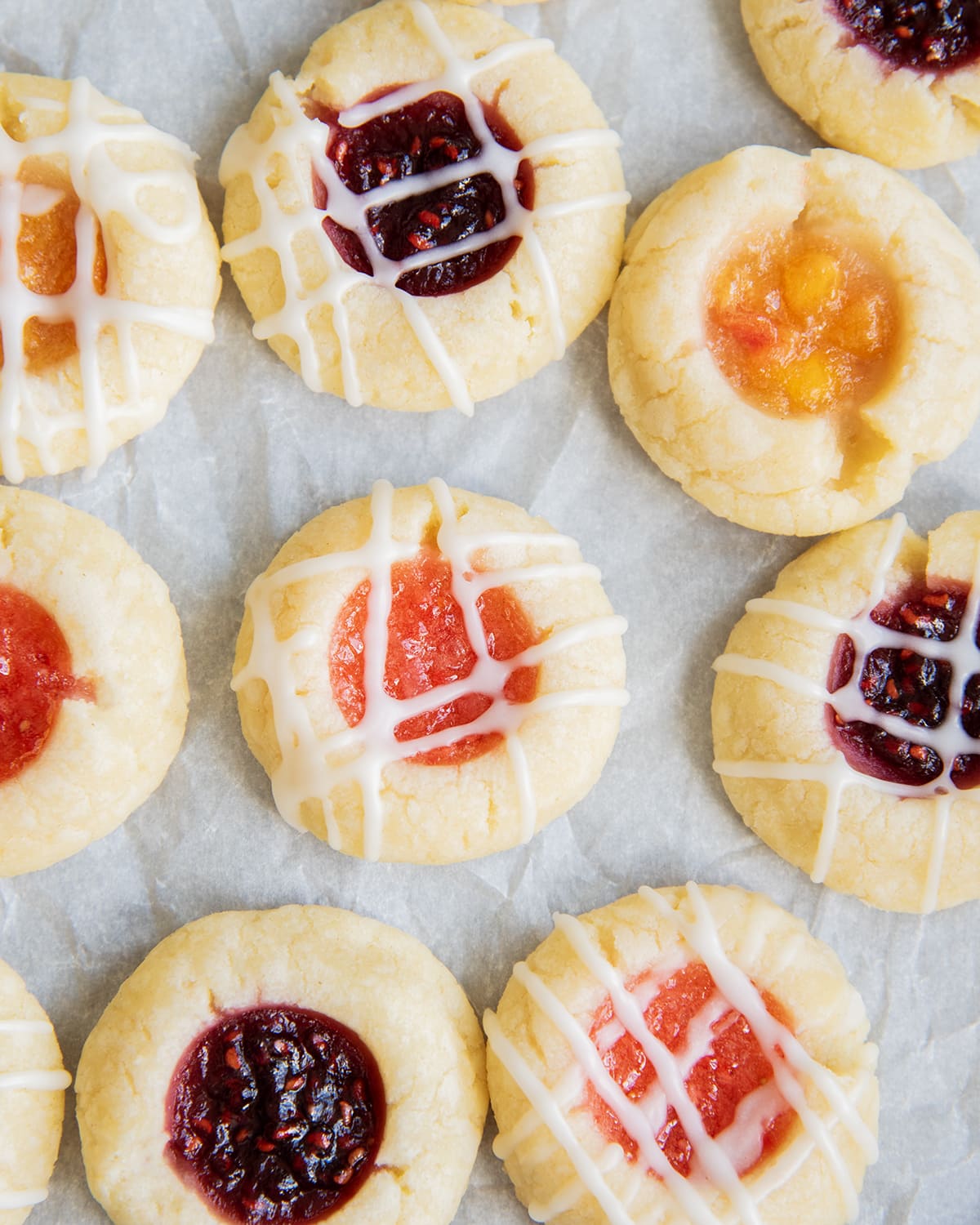 Thumbprint jam cookies filled with a variety of jams on a piece of parchment paper.