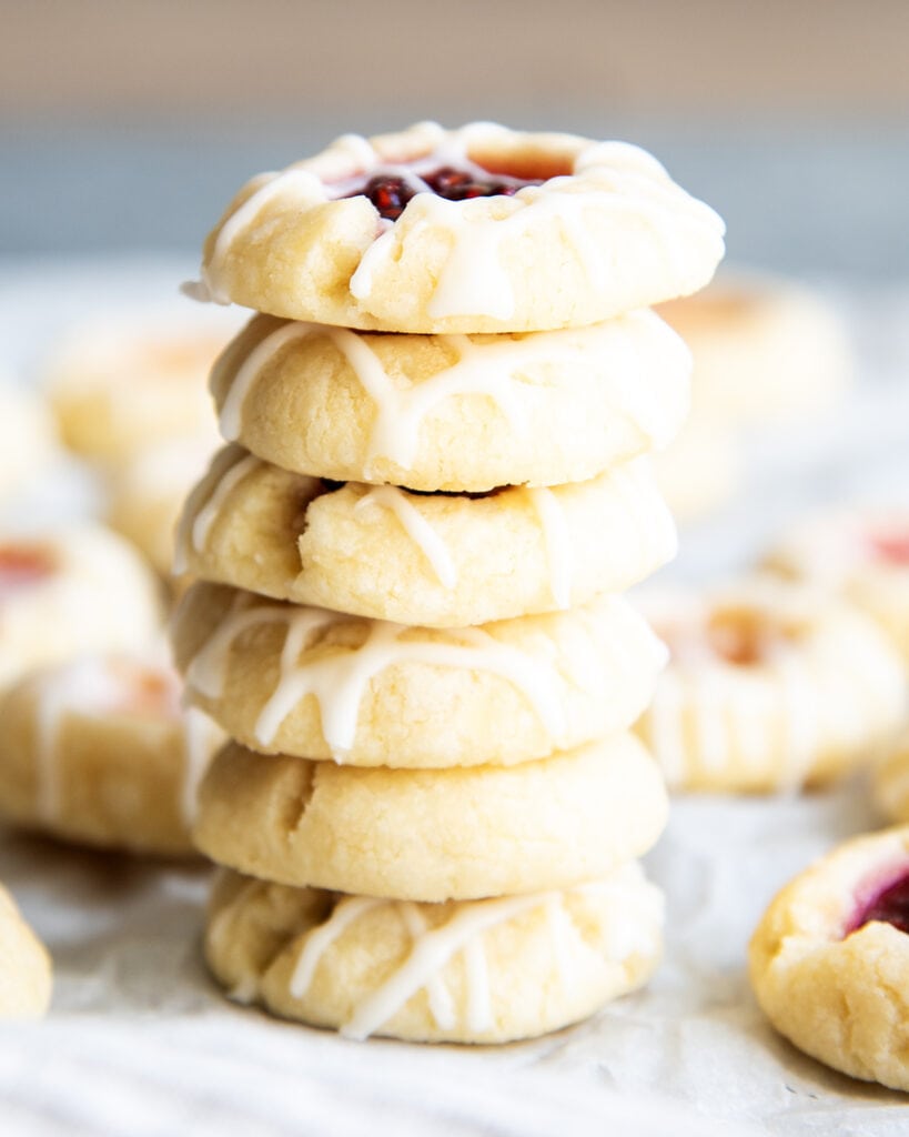 A stack of 6 thumbprint cookies filled with jam, and drizzled with a vanilla icing.