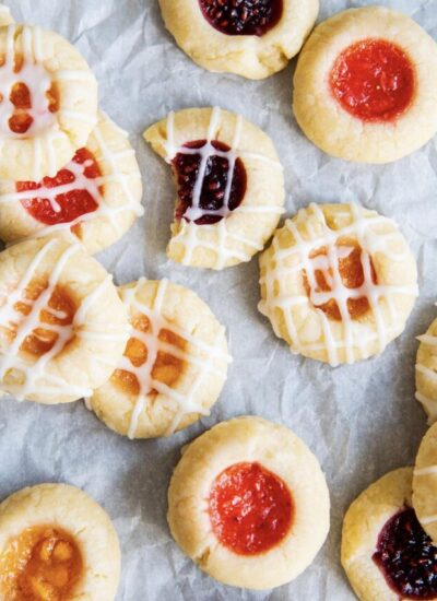 Thumbprint cookies filled with jam and randomly scattered on a piece of parchment paper.