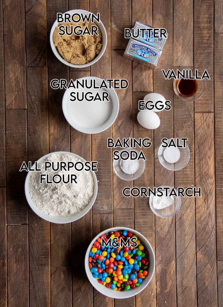 Bowls of the ingredients needed to make m&m cookies, like flour, brown sugar, baking soda, m&ms, etc.