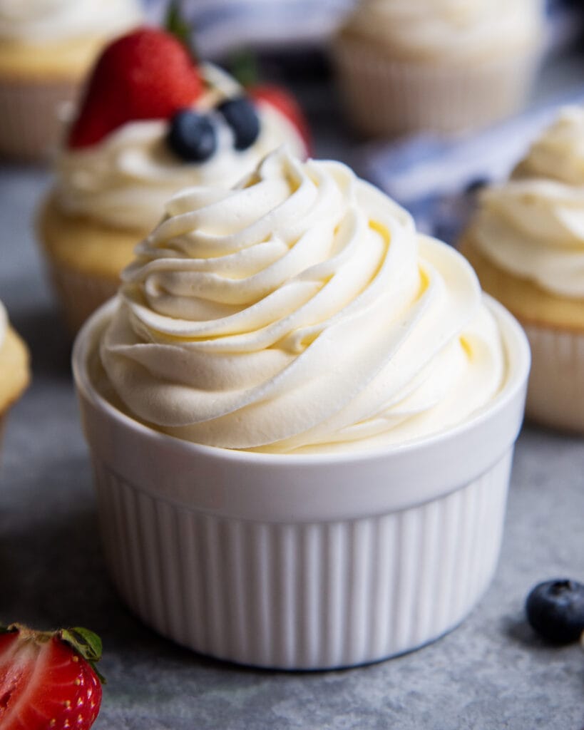 A ramekin bowl full of cream cheese whipped cream frosting, piped above the top of it.