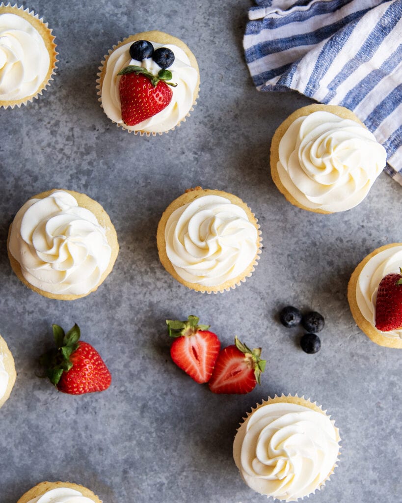 An overhead photo of cupcakes topped with piped whipped cream cheese frosting.