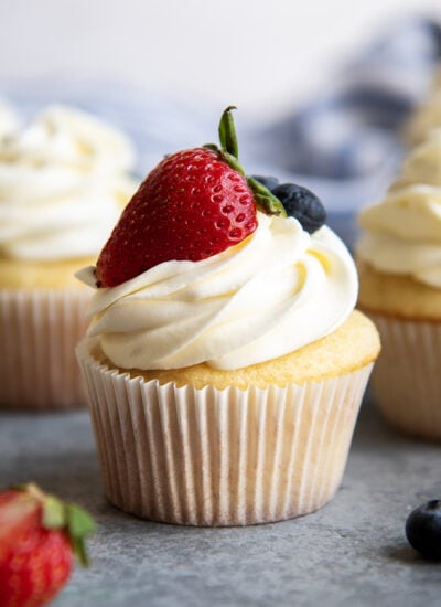 A cupcake topped with cream cheese and whipped cream frosting and half a strawberry with leaves on it.