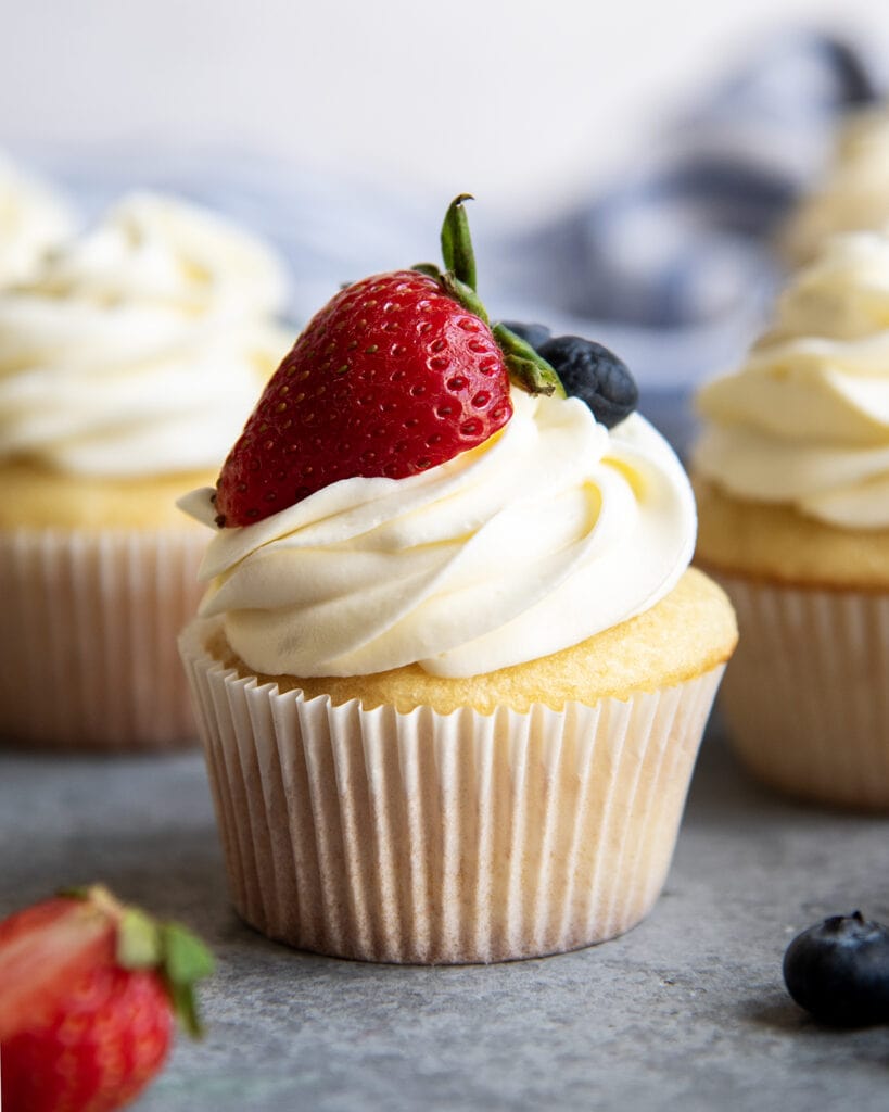 A cupcake topped with cream cheese and whipped cream frosting and half a strawberry with leaves on it.