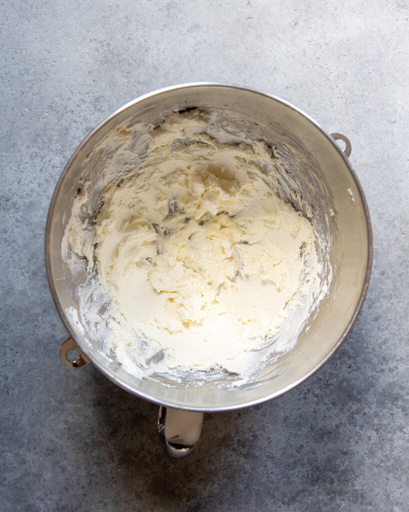 A stand mixer bowl with cream cheese beaten in it.