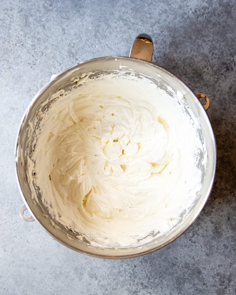 A metal stand mixer bowl with whipped cream cheese frosting in it.