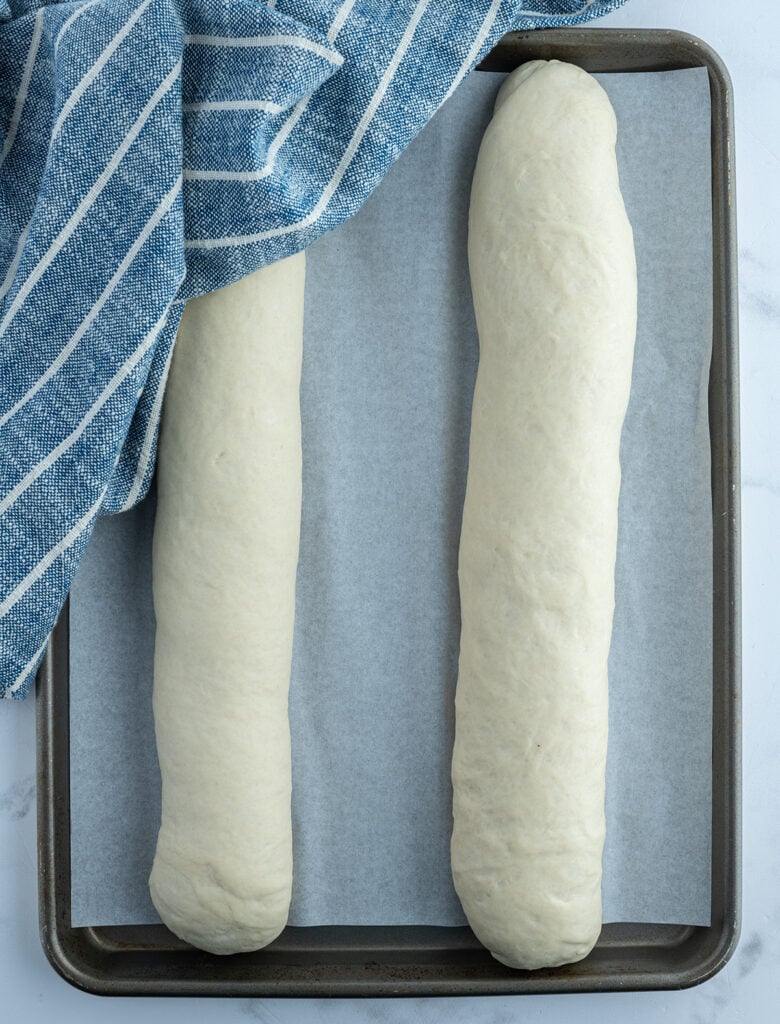 To raw loaves of bread on a pan.