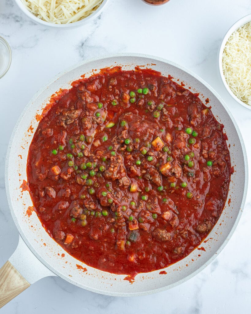 A white pan with a tomato sauce full of vegetables and meat.