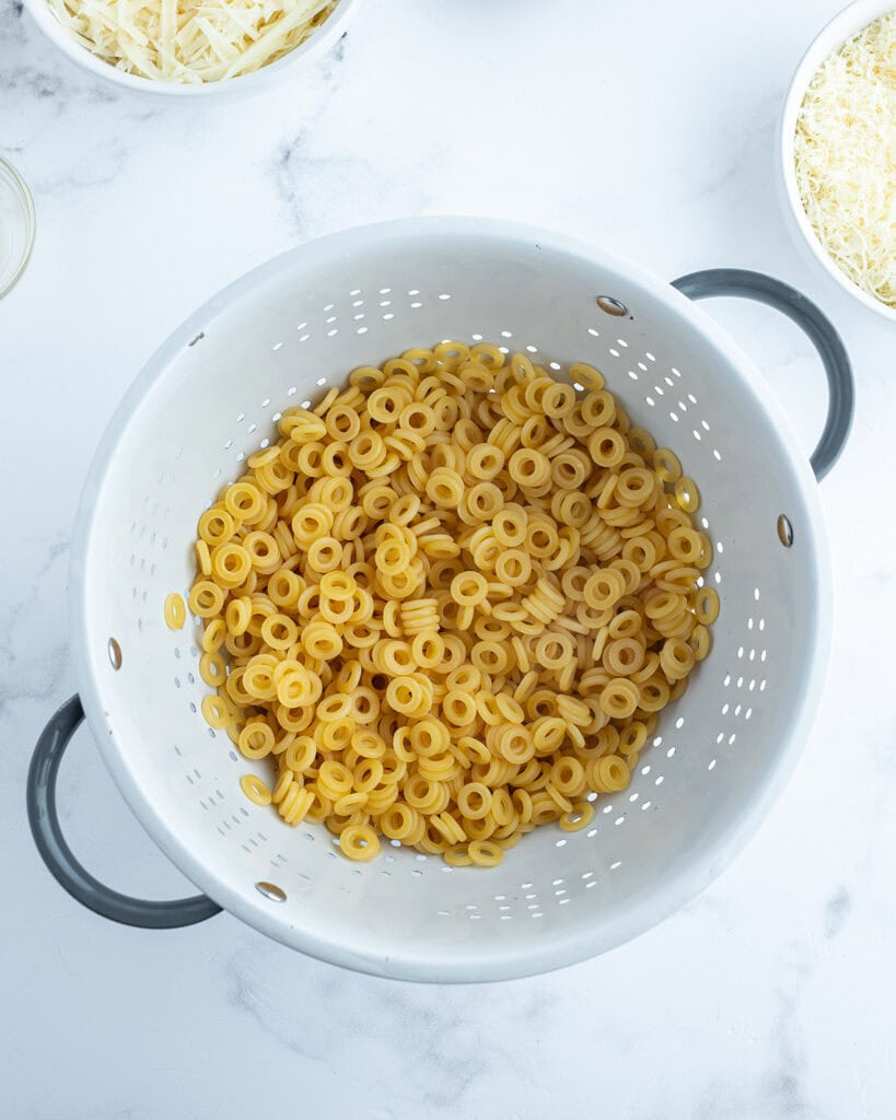 A white colander full of ring shaped pasta noodles.