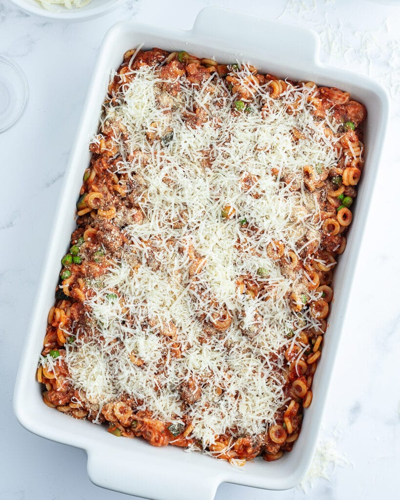 A rectangle baking dish full of pasta and topped with shredded cheese.