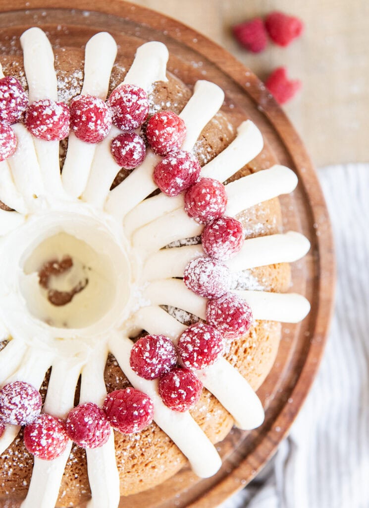 An above view of a bundt cake topped with stripes of cream cheese frosting and fresh raspberries.