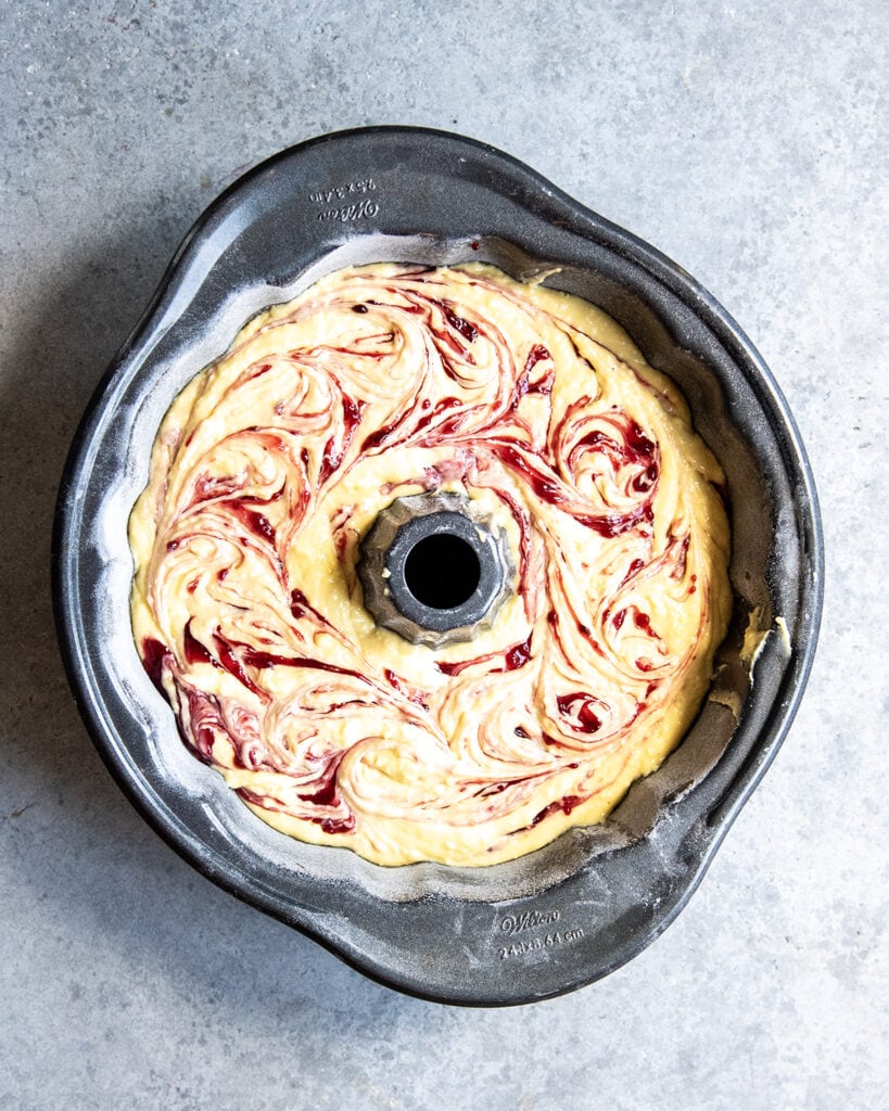 A cake batter swirled with raspberry pie filling in a bundt cake pan.
