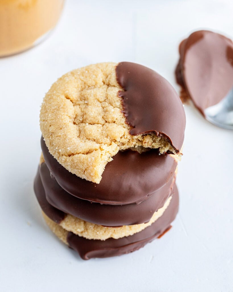 A stack of peanut butter cookies that are dipped in chocolate, and the top cookie has a bite taken out of it.