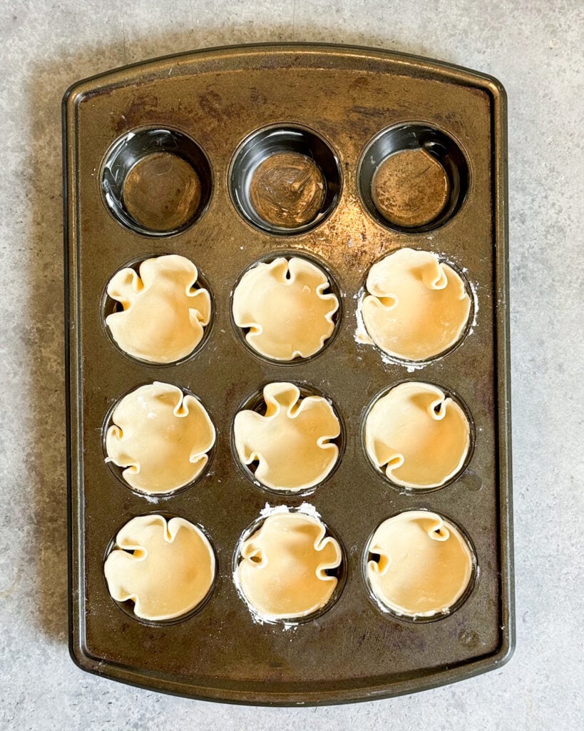 A muffin pan lined with mini pie crusts.