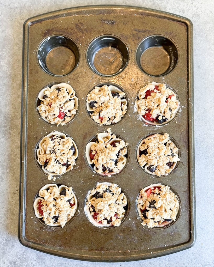Mini pies in a muffin tin topped with streusel topping.
