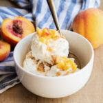 A bowl of peach pie ice cream topped with fresh peach pieces.