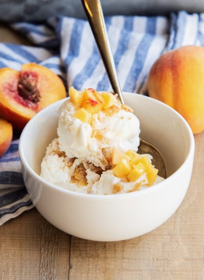 A bowl of peach pie ice cream topped with fresh peach pieces.